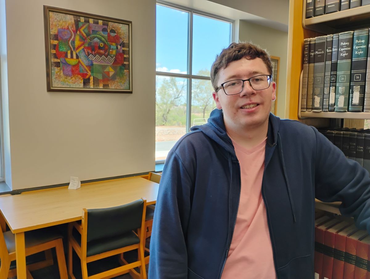 Nicholas standing in the library smiling at the camera.